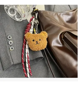 Detailed view of a brown plush bear charm with woven lanyard on a dark brown leather bag