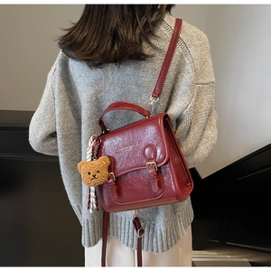Detail of burgundy pleated leather backpack featuring metallic buckles and bear pendant