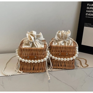Close-up of woven straw bucket bag with pearl handle and metal chain on a marble surface