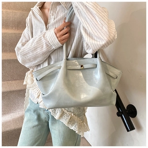 Detail of light blue glossy leather tote bag with gold metal buckle on casual outfit