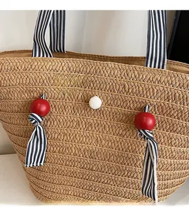Close-up of woven straw tote bag with striped fabric handle and red bead charm