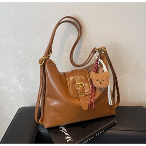 Detail view of a vintage brown leather tote bag featuring a cute plush bear charm and woven rope