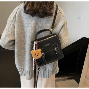 Close-up of black glossy PU leather handbag with silver buckles and a cute bear charm