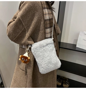 Gros plan du sac en peluche gris avec pendentif poupée marron et fine bandoulière blanche