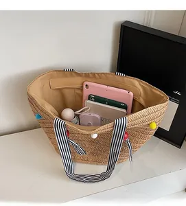 Detailed interior view of a large woven straw beach tote bag with vibrant pom-poms