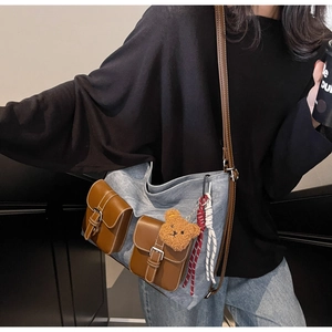 Detail of grey-blue denim tote bag with brown leather pockets and plush bear charm