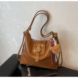 Detail view of brown vintage leather tote with buckle strap and a cute bear charm
