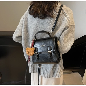 Model wearing a black glossy faux leather crossbody bag with a plush bear keychain