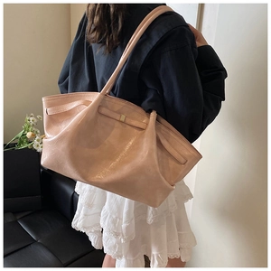 Close-up of pleated beige tote bag with metallic buckle and glossy finish on model's shoulder
