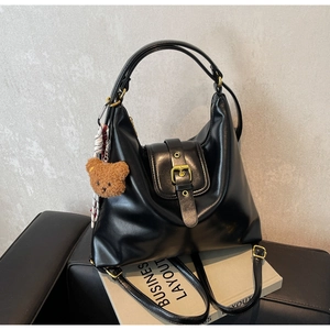Detail of black leather hobo bag featuring a gold buckle and cute brown bear charm
