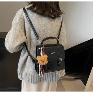 Detail of a chic black glossy leather handbag featuring a plush teddy bear charm