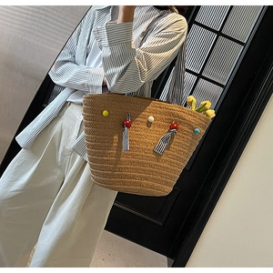 Straw tote bag detail with colorful pom-poms and black and white striped ribbons