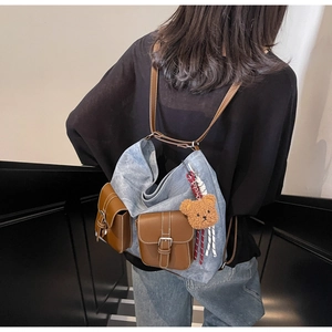 Detail view of the patchwork denim and brown leather backpack on model with bear charm