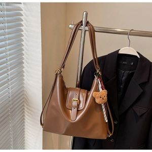Brown leather tote bag featuring golden metal buckle detail and cute plush bear charm