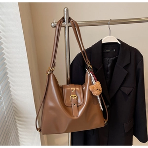 Detail of a brown leather tote bag with metal buckle and a cute teddy bear charm on a hanger