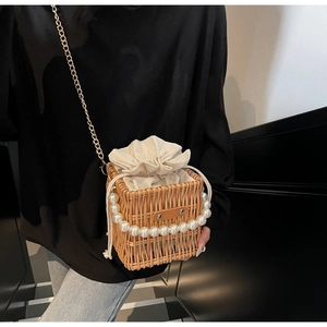 Macro detail of hand-woven straw bucket bag with pearl handle and gold chain strap