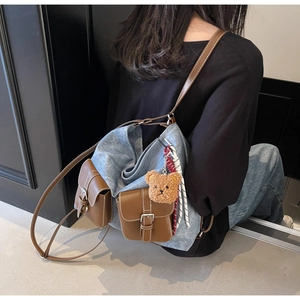 Detail of blue denim crossbody bag with brown leather pockets and a cute bear charm