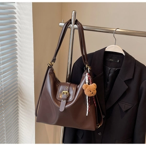 Close-up of vintage brown leather tote bag with gold buckle and plush bear charm accessory