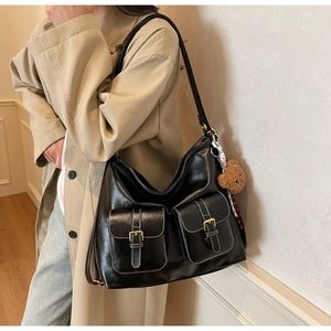 Detail of a black faux leather tote with white stitching and plush bear charm