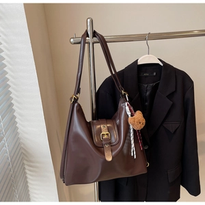 Detail of dark brown leather tote bag with metal buckle and plush bear charm on hanger