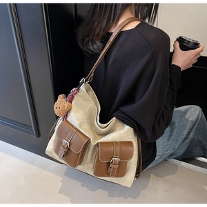 Detail of beige canvas tote bag with brown leather pockets and a small bear pendant