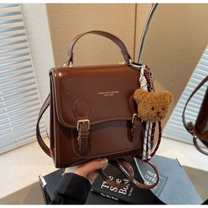 Macro detail of vintage brown leather handbag with fashion logo and plush bear charm