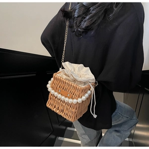 Detailed close-up of straw bucket bag with pearl handle and golden chain strap