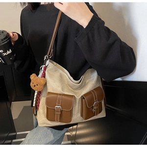 Detail view of large canvas tote bag with brown leather pockets and teddy bear charm