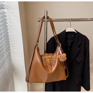 Brown leather hobo shoulder bag with metal buckle and plush bear charm on a suit