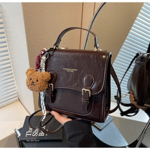 Detailed view of dark brown oil wax leather handbag with retro buckles and bear charm