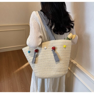 Detailed view of beige woven straw tote bag with colorful pom-poms and striped straps