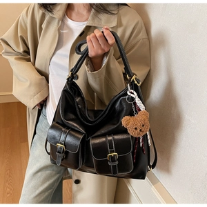 Close-up of black retro tote bag featuring double buckled pockets and a plush bear charm
