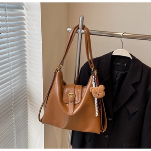 Detail view of large caramel faux leather tote with metal buckle and teddy bear charm