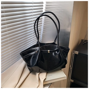 Detail of a large black glossy patent leather tote bag with metallic buckle and shoulder strap