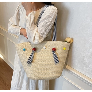 Detail of hand-woven straw tote bag featuring colorful pompoms and striped ribbon accents