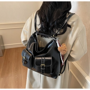 Close-up of black faux leather backpack with white stitching and metal buckle pockets