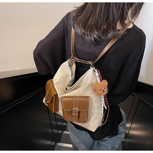 Detail of canvas backpack with brown leather pockets and a small plush bear charm attached