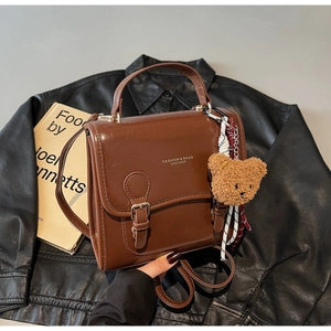 Detail view of a vintage brown leather handbag with a metal buckle and a plush bear charm