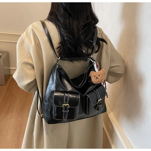 Detail of black leather multi-pocket tote bag with white stitching and bear charm