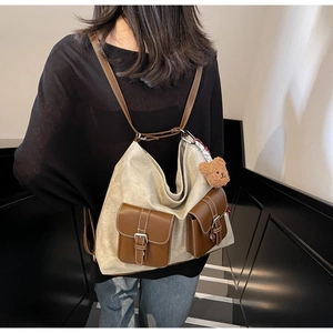 Detail of canvas backpack with brown leather pockets and a small plush bear pendant