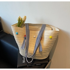 Detail of woven straw tote bag with colorful pom-poms and striped ribbon handles