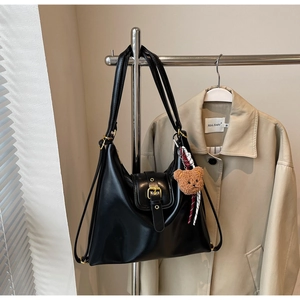 Detail of vintage black leather tote bag with gold buckle and cute brown bear charm