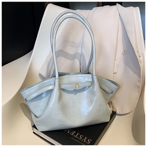 Detail of light blue wrinkled tote bag with golden buckle and leather strap on a book