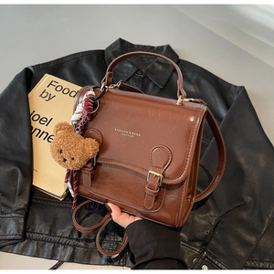 Macro shot of retro brown leather handbag with gold logo and plush bear charm on jacket