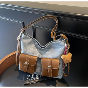 Close-up of blue denim tote bag with brown leather pockets and a cute bear charm