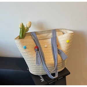Macro view of interior lining and capacity of straw tote bag with colorful pom-poms