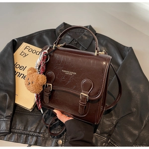 Detail view of brown leather handbag with plush bear charm and plaid silk scarf decoration
