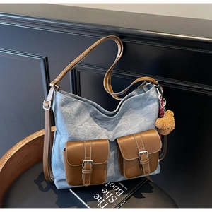 Close-up of vintage denim tote bag with leather pockets, buckles, and plush bear charm