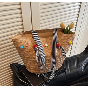 Detail of woven straw tote bag featuring colorful pom-poms and striped fabric handles