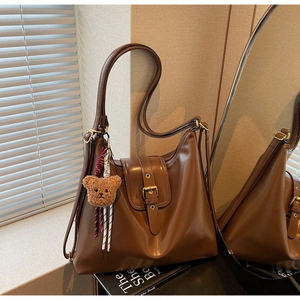 Detail of vintage brown leather tote bag with metal buckle and cute plush bear charm